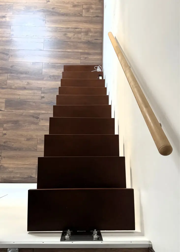 Escalier en bois sombre vu de haut avec rampe claire.