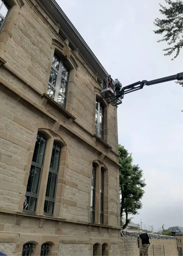 Travailleur dans une nacelle inspectant un bâtiment en pierre.