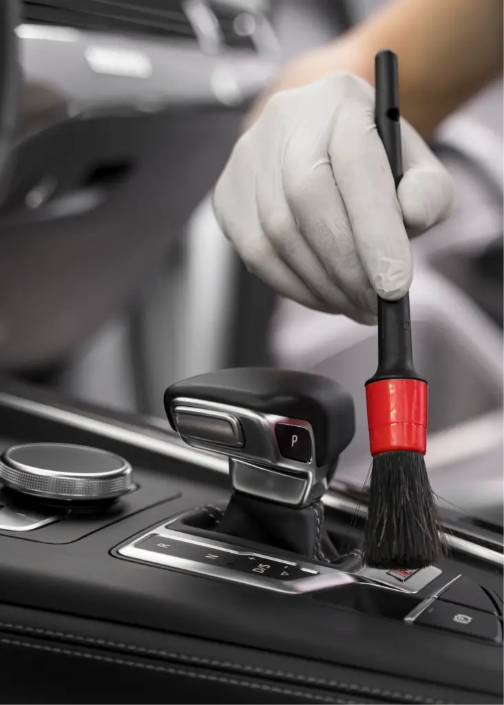 Main gantée nettoyant la console centrale d'une voiture avec pinceau.