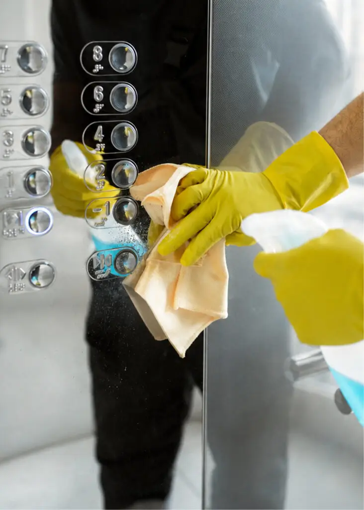 Nettoyage des boutons d'un ascenseur avec des gants jaunes.
